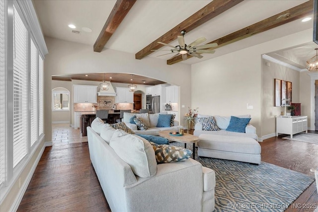 living room with beam ceiling, baseboards, ceiling fan, dark wood-style floors, and arched walkways