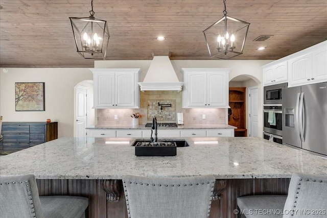 kitchen with appliances with stainless steel finishes, arched walkways, a chandelier, custom range hood, and visible vents