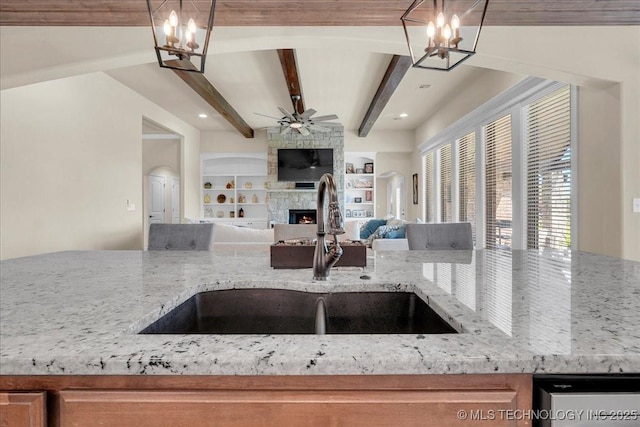 kitchen featuring a fireplace, light stone countertops, open floor plan, a sink, and ceiling fan with notable chandelier