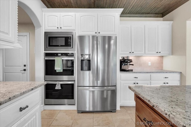 kitchen with appliances with stainless steel finishes, light stone counters, arched walkways, white cabinetry, and backsplash