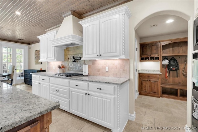 kitchen featuring crown molding, custom exhaust hood, light stone counters, backsplash, and stainless steel gas stovetop