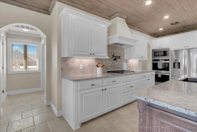 kitchen featuring backsplash, crown molding, appliances with stainless steel finishes, baseboards, and custom exhaust hood
