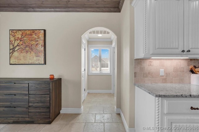 hall with crown molding, visible vents, stone tile flooring, baseboards, and arched walkways