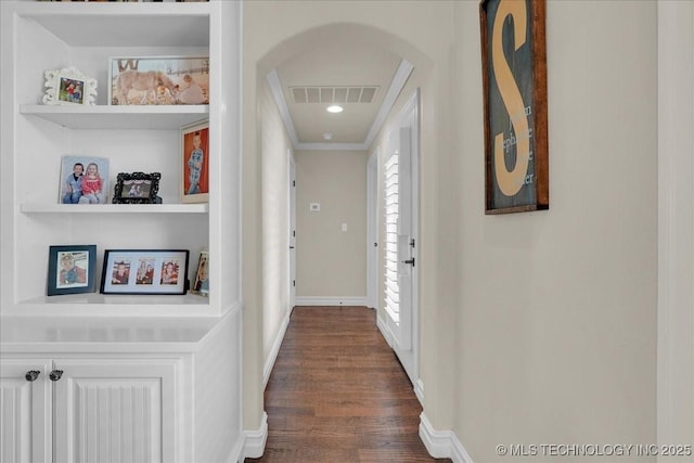hallway featuring visible vents, crown molding, arched walkways, baseboards, and dark wood-style floors