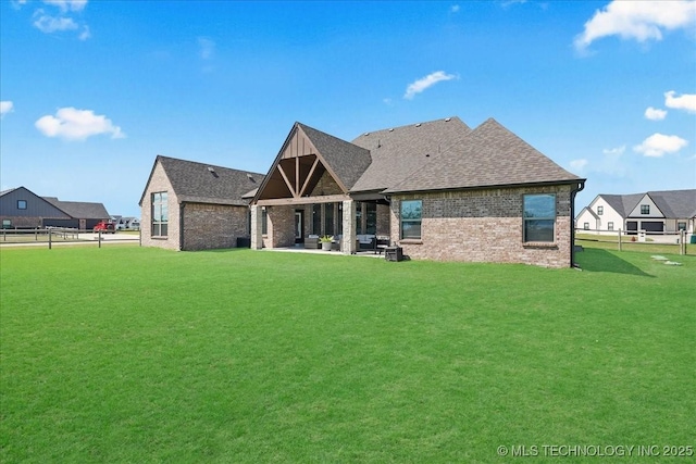 rear view of house featuring a lawn, a patio area, brick siding, fence, and a shingled roof
