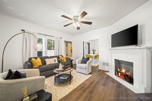 living room featuring ceiling fan, a textured ceiling, wood finished floors, a tile fireplace, and visible vents