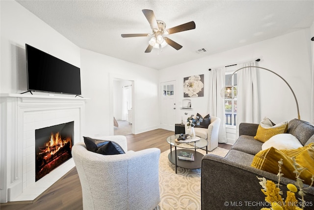 living room with ceiling fan, a tile fireplace, wood finished floors, and visible vents