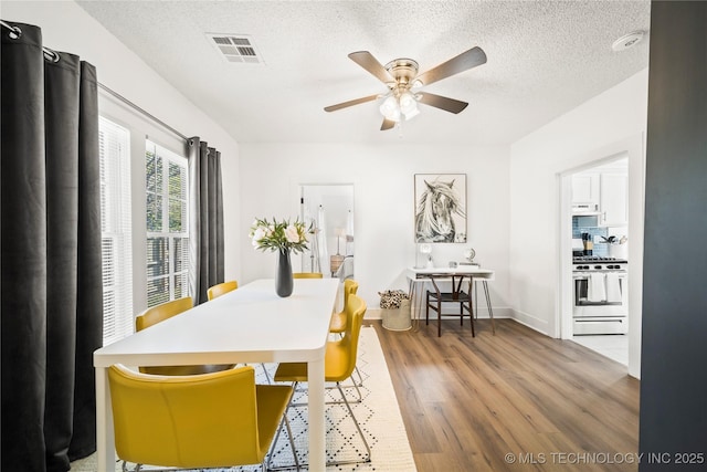 dining space with a textured ceiling, a ceiling fan, baseboards, wood finished floors, and visible vents