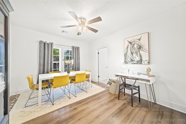 dining space with a textured ceiling, a ceiling fan, baseboards, wood finished floors, and visible vents