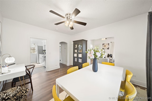 dining space featuring arched walkways, baseboards, a ceiling fan, and dark wood finished floors