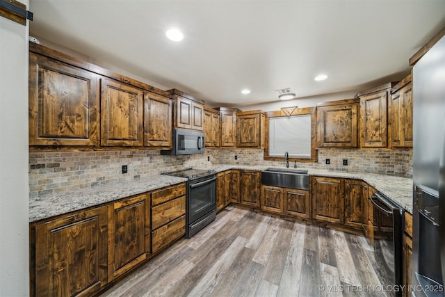 kitchen with wood finished floors, black electric range, tasteful backsplash, light stone counters, and a sink