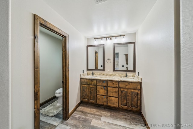 bathroom with double vanity, toilet, a sink, and wood finished floors