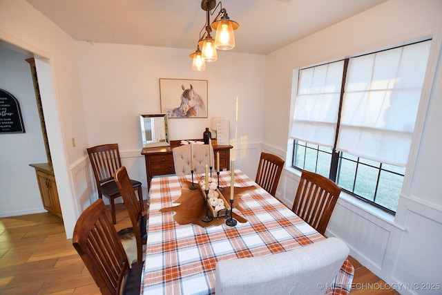 dining area with light wood-type flooring, wainscoting, and a decorative wall