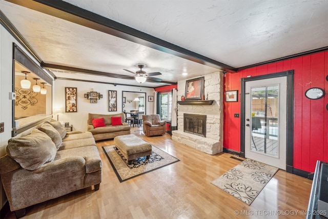 living room with beam ceiling, a stone fireplace, a ceiling fan, wood finished floors, and visible vents