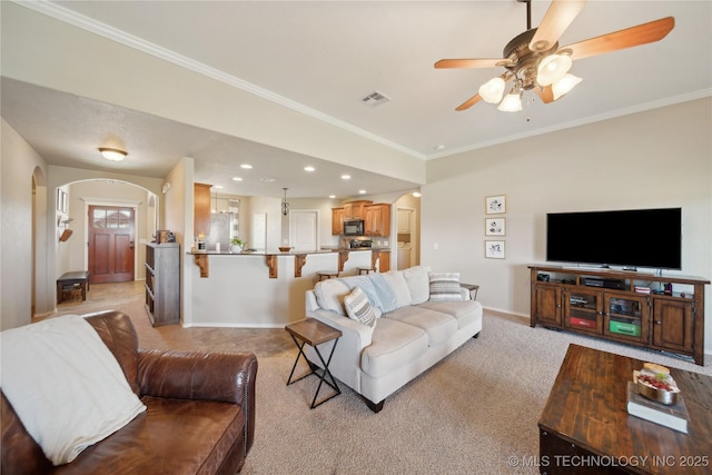 living area featuring a ceiling fan, light colored carpet, arched walkways, baseboards, and ornamental molding