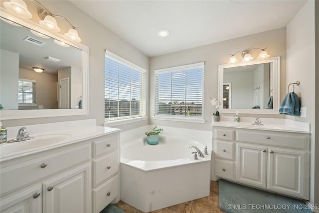 bathroom with visible vents, two vanities, a sink, and a bath