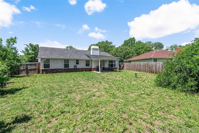 rear view of property with a patio, a fenced backyard, a chimney, brick siding, and a yard