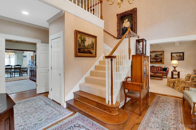 stairs with recessed lighting, ornamental molding, wood finished floors, and a notable chandelier