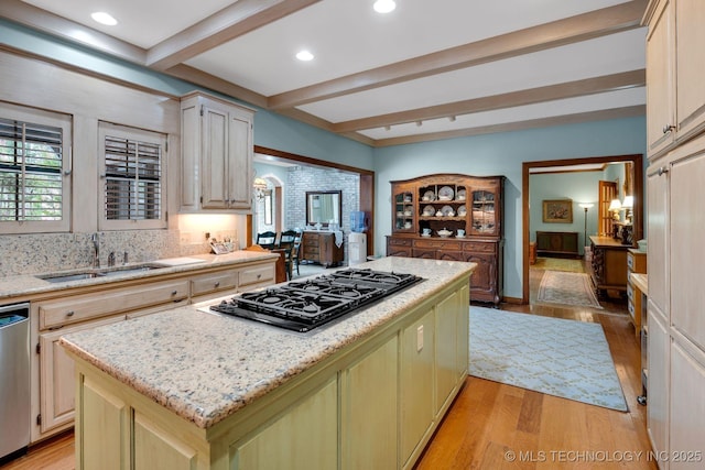 kitchen with a sink, beamed ceiling, a kitchen island, and black gas stovetop
