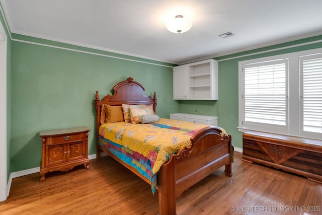 bedroom featuring baseboards, visible vents, ornamental molding, and light wood-style floors