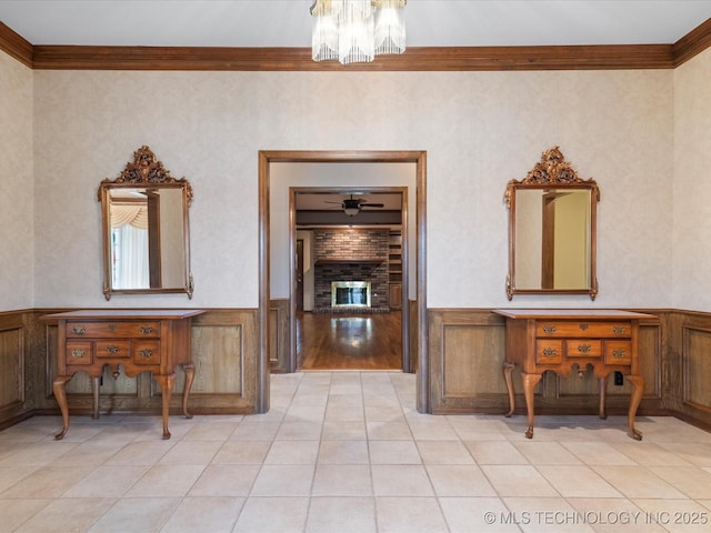 hallway featuring crown molding, light tile patterned flooring, a wainscoted wall, and a notable chandelier