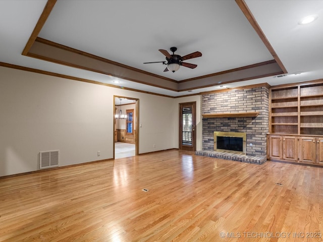 unfurnished living room with visible vents, crown molding, a fireplace, a raised ceiling, and ceiling fan with notable chandelier