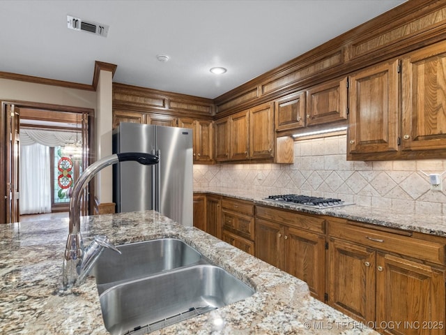 kitchen featuring visible vents, brown cabinetry, tasteful backsplash, a sink, and stainless steel appliances