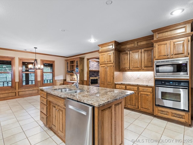 kitchen featuring a kitchen island with sink, brown cabinets, a sink, backsplash, and stainless steel appliances