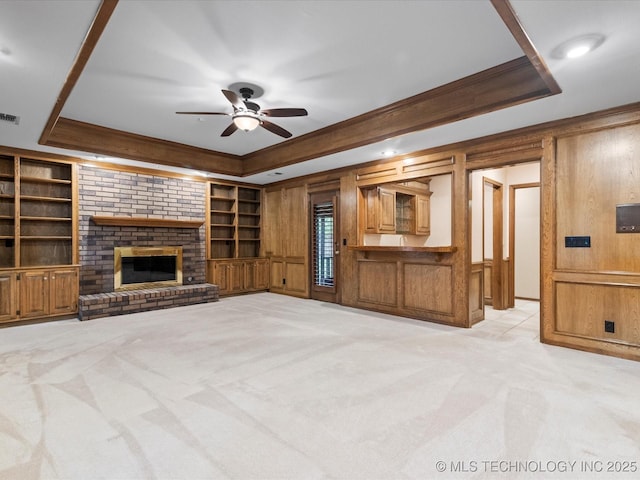 unfurnished living room featuring ceiling fan, light colored carpet, a raised ceiling, built in features, and visible vents