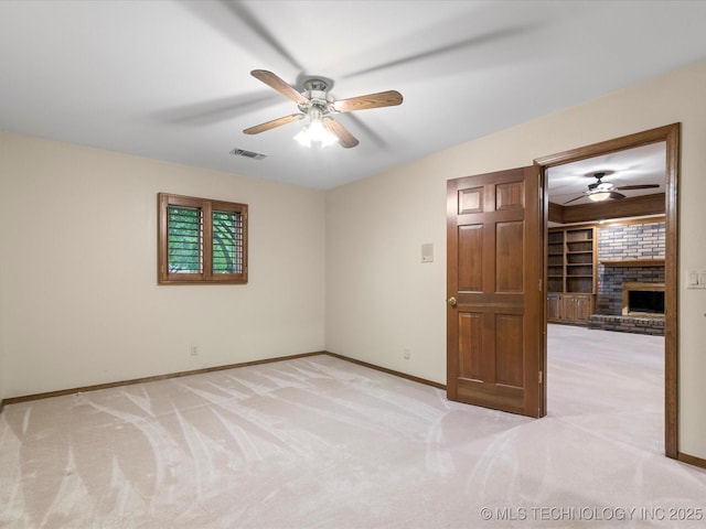 empty room with a fireplace, a ceiling fan, light colored carpet, and visible vents