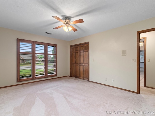 unfurnished bedroom featuring a closet, visible vents, light carpet, baseboards, and ceiling fan