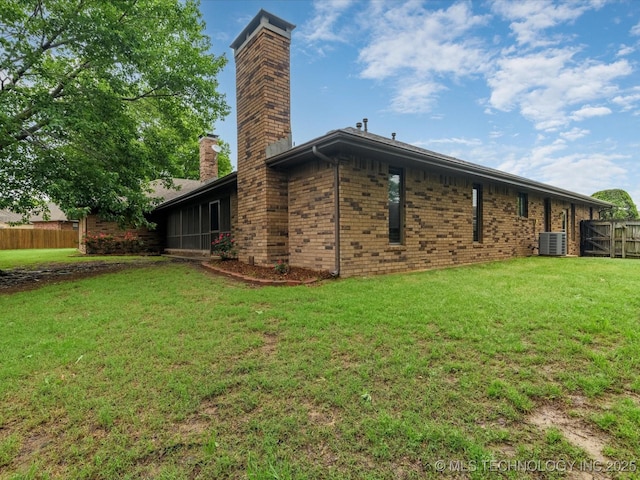 back of house with fence, brick siding, central AC unit, a chimney, and a yard