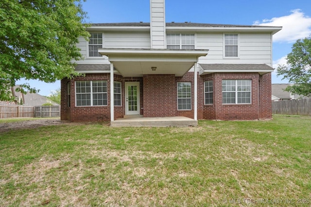 back of house with fence, a chimney, brick siding, a patio area, and a lawn