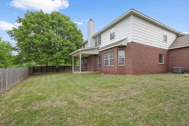 back of property with a fenced backyard, a chimney, brick siding, central AC unit, and a yard