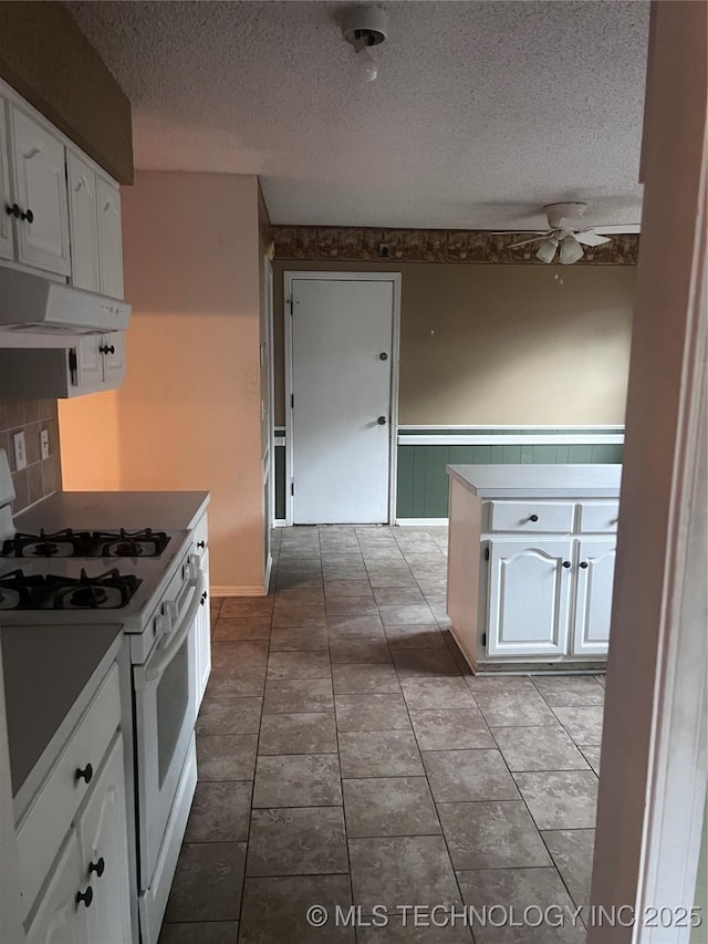kitchen featuring a ceiling fan, a textured ceiling, under cabinet range hood, white gas range, and white cabinets