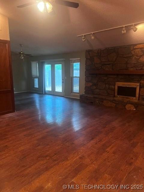 unfurnished living room featuring track lighting, a fireplace, a ceiling fan, and wood finished floors