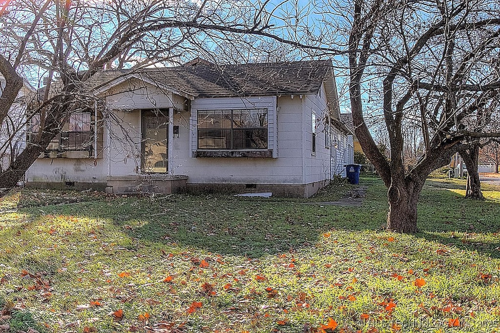 bungalow-style house with a shingled roof, a front lawn, and crawl space