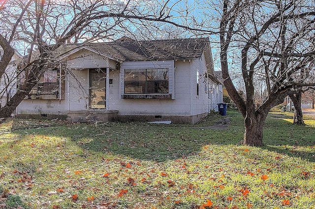 bungalow-style house with a shingled roof, a front lawn, and crawl space