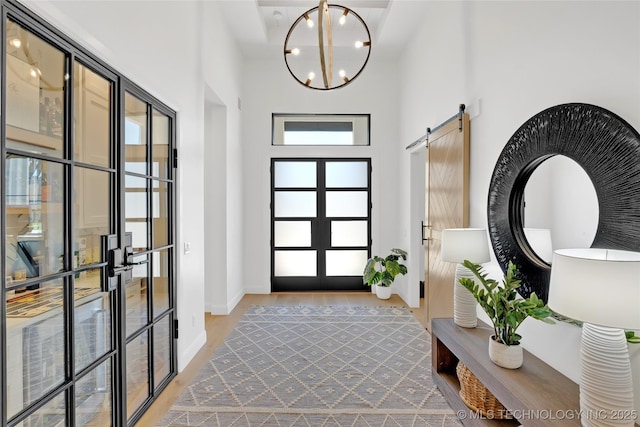 entryway featuring a barn door, a chandelier, light wood-style flooring, baseboards, and a towering ceiling