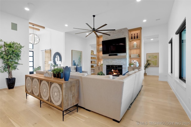 living area with a fireplace, baseboards, recessed lighting, a ceiling fan, and light wood-style flooring