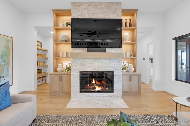 living area with a stone fireplace, a ceiling fan, light wood-style flooring, and baseboards