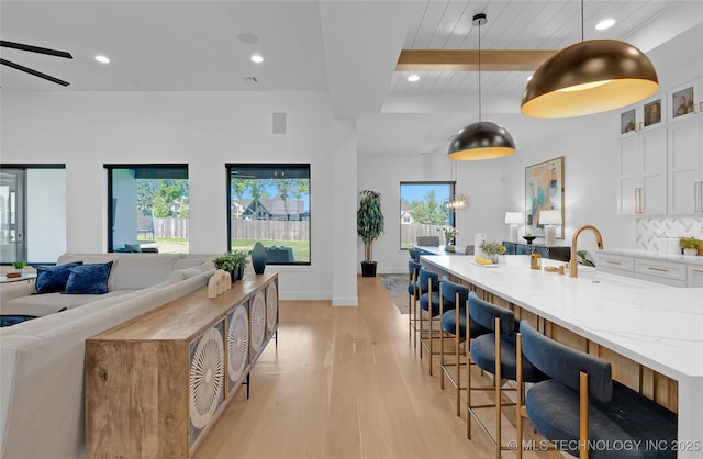 kitchen with beam ceiling, light stone countertops, open floor plan, white cabinetry, and light wood finished floors