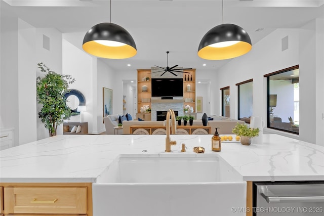 kitchen with light stone counters, open floor plan, a sink, and a ceiling fan