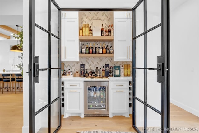 bar featuring indoor wet bar, backsplash, light wood-type flooring, and beverage cooler