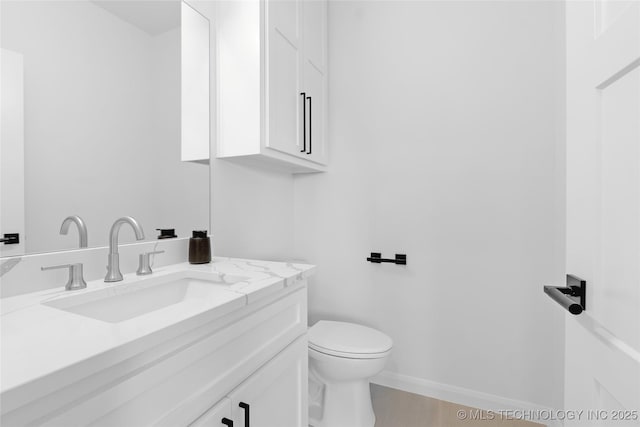 half bath with toilet, baseboards, and vanity