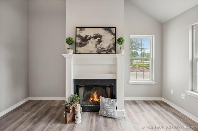 unfurnished living room with baseboards, vaulted ceiling, a glass covered fireplace, and wood finished floors