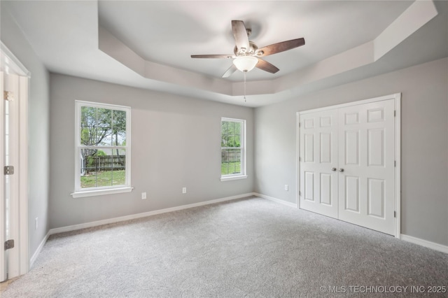 unfurnished bedroom with a tray ceiling, baseboards, multiple windows, and carpet flooring