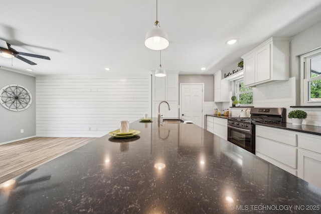 kitchen featuring decorative backsplash, white cabinets, a ceiling fan, gas stove, and decorative light fixtures