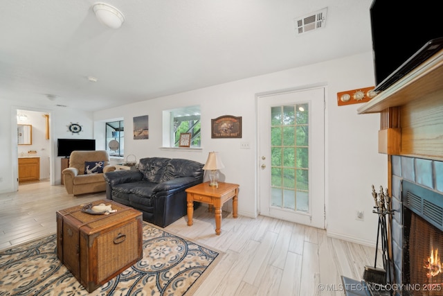 living room with plenty of natural light, a lit fireplace, light wood-type flooring, and visible vents