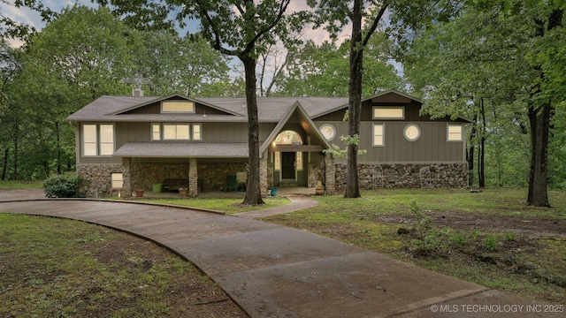 view of front facade with a shingled roof, a front yard, driveway, and stone siding
